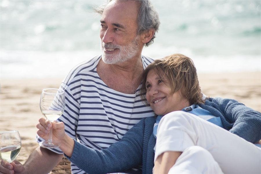 Smiling senior couple with white wine on a beach
