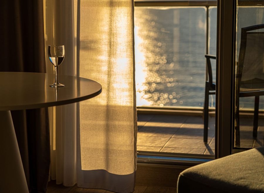 Sunlight on the sea through a balcony door, a wine glass on the table