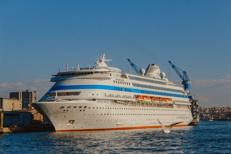 White cruise ship moored in a harbor with cranes behind